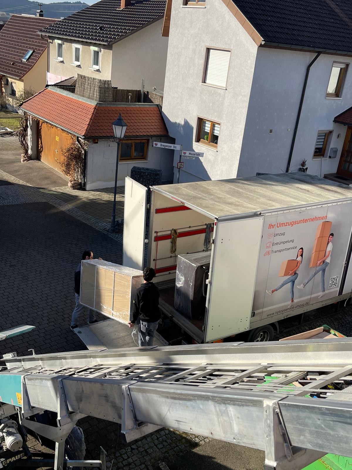 Umzugsfirma Konstanz: Team verlaedt ein geschuetztes Moebelstueck sicher in den Umzugswagen, Moebellift im Vordergrund