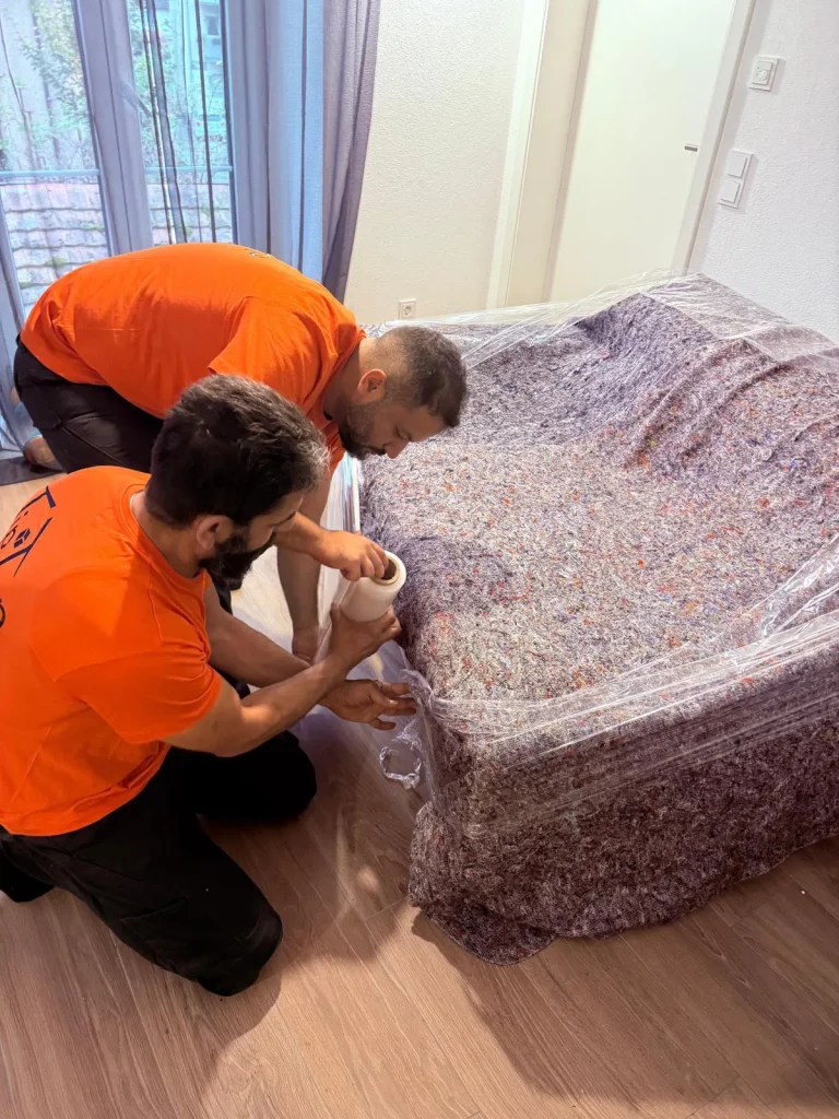 Zwei Umzugshelfer von TipTop Move verpacken ein Möbelstück mit einer Schutzdecke