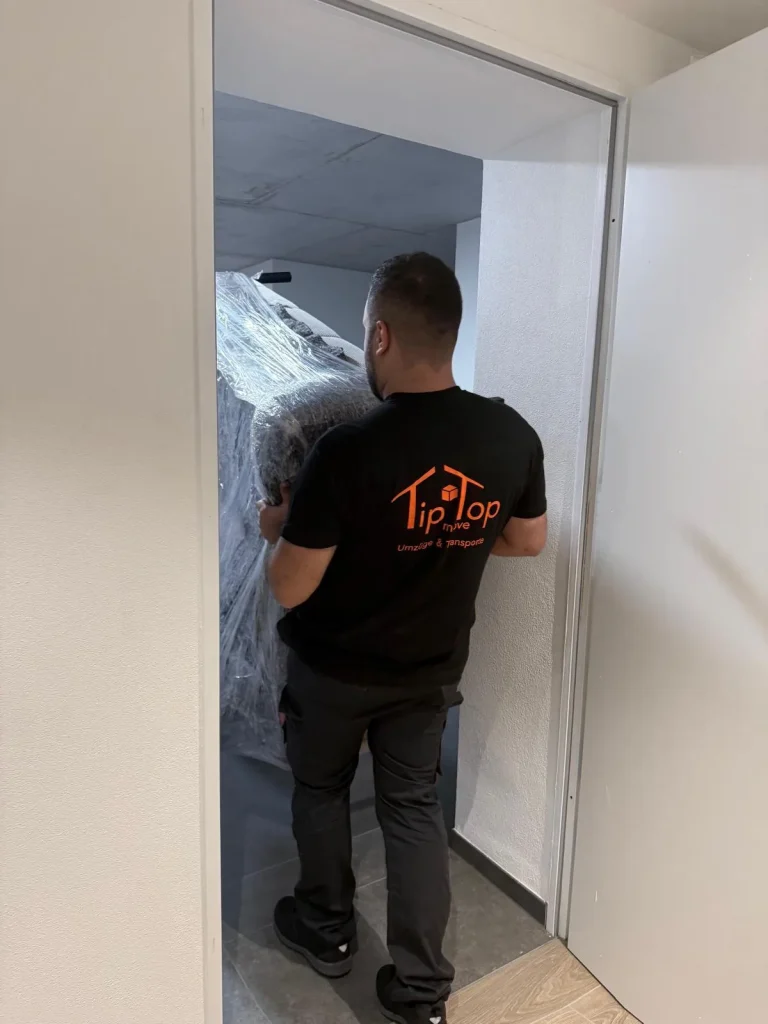 Umzugshelfer von TipTop Move trägt ein verpacktes Möbelstück aus der Wohnung